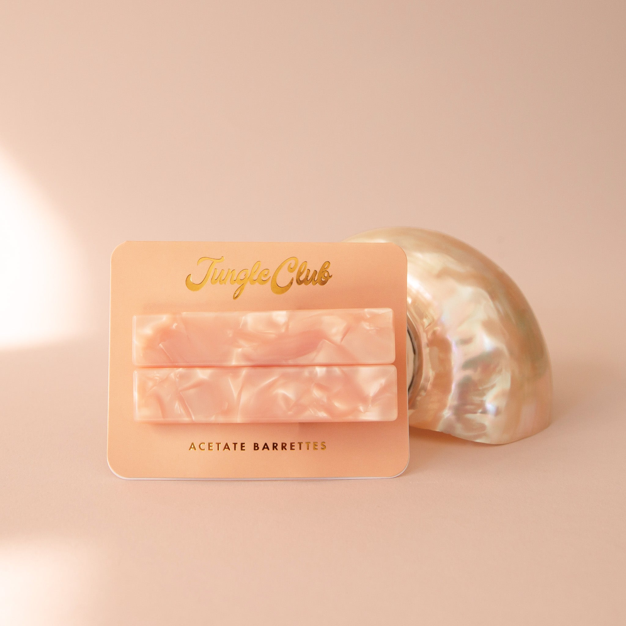 Pink pearl detailed hair barrettes on a coral colored piece of paper and a shell behind.