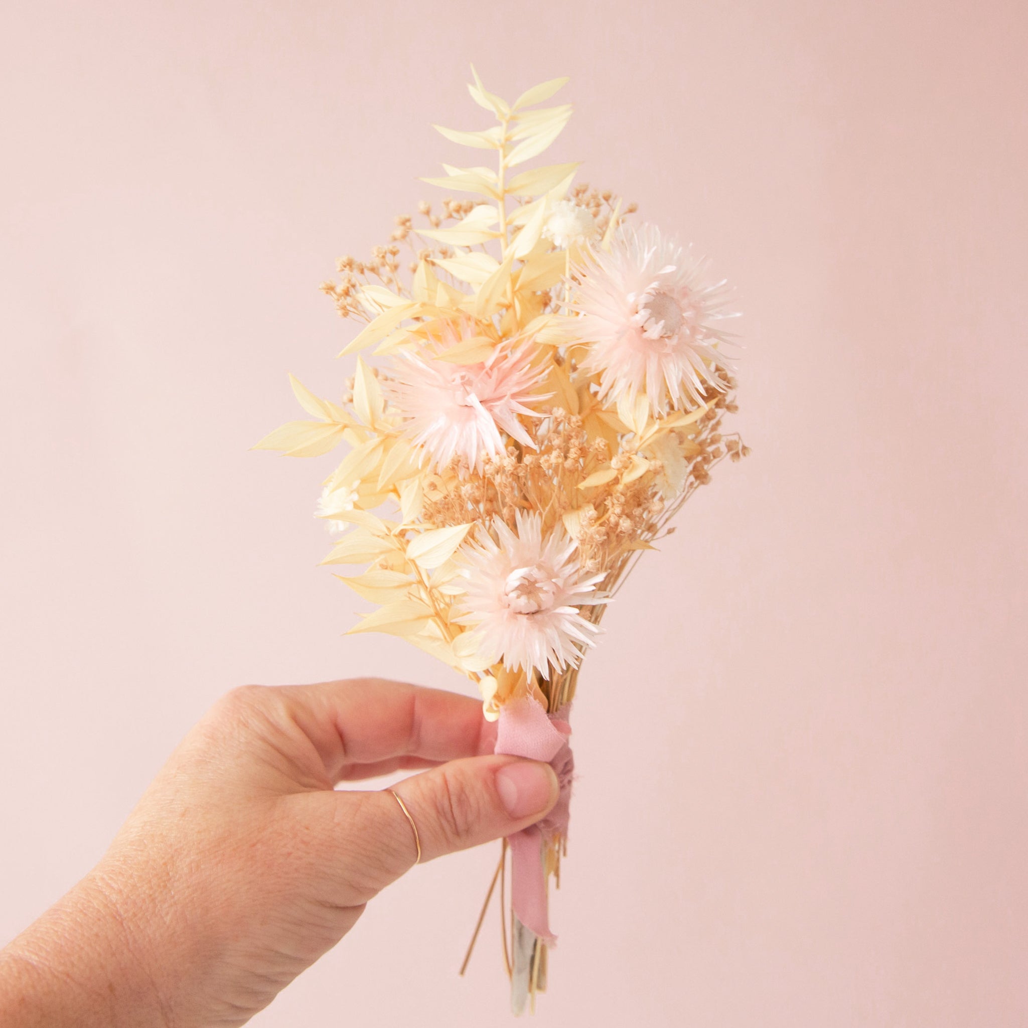 A bouquet of dried florals with tan and pink flowers tied with a pink bow. 