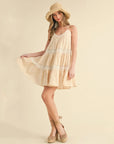 A cream tiered mini dress with spaghetti straps and lace details.