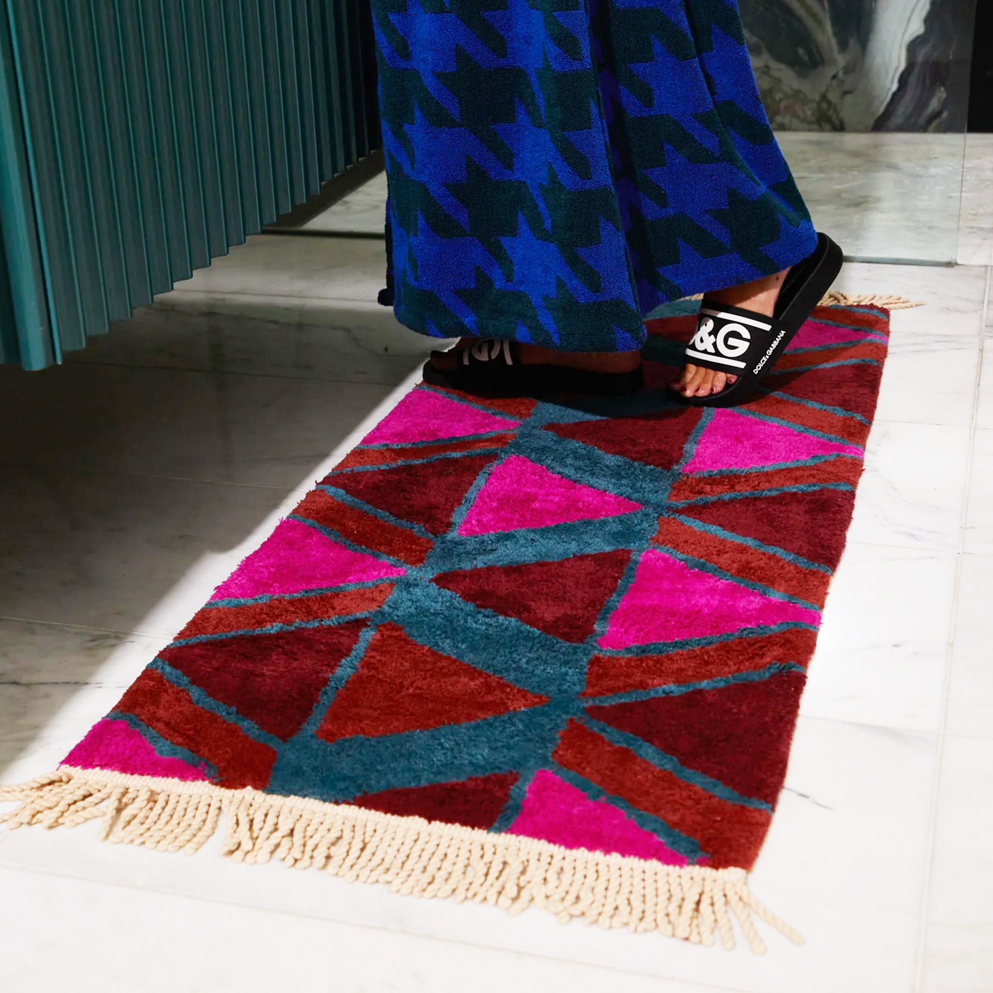 A pink, red, rust and teal triangle patterned bath mat with tassel details on the two ends.