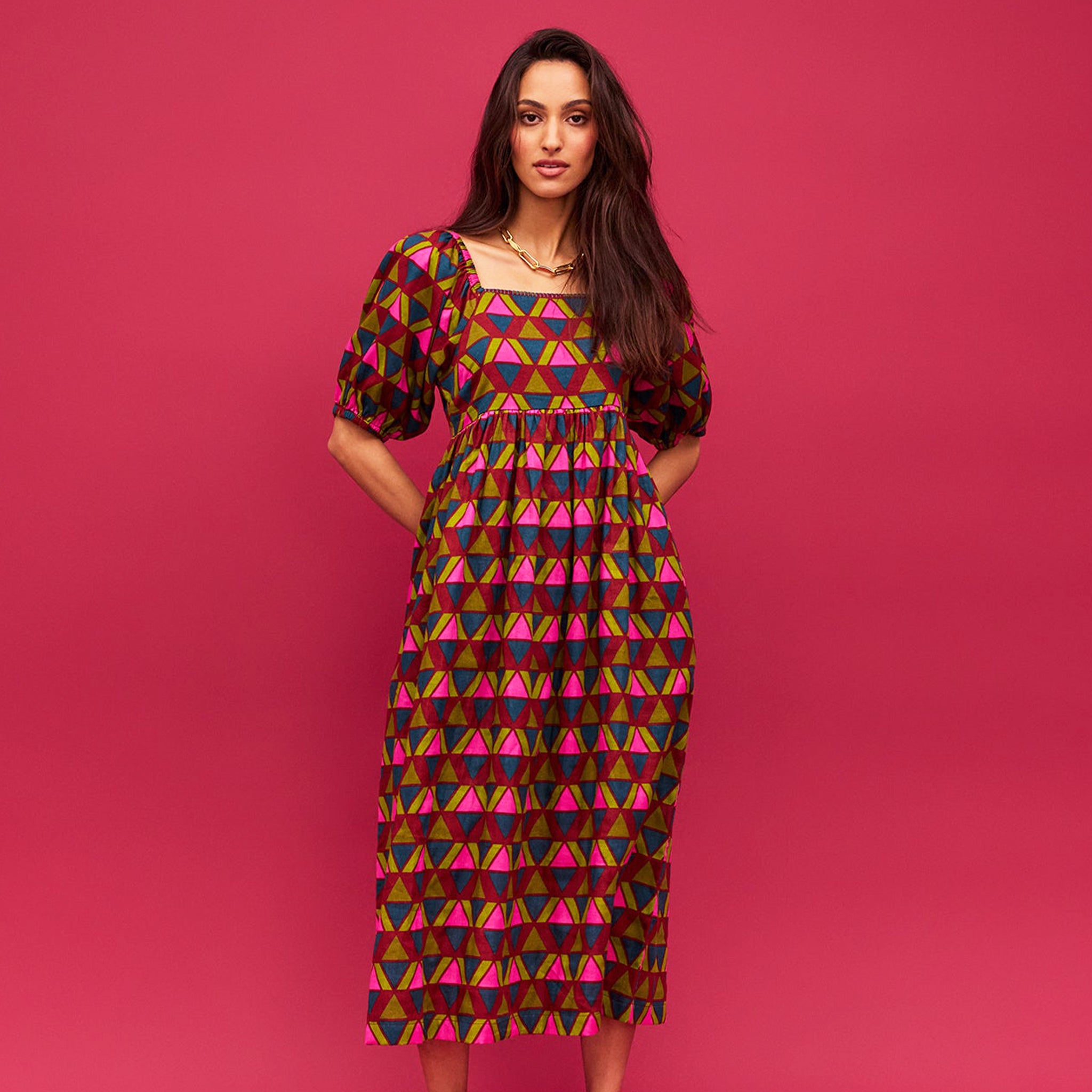 A pink, green, teal and red triangle patterned maxi dress with a square neckline, pockets and puff sleeves. 