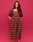 A pink, green, teal and red triangle patterned maxi dress with a square neckline, pockets and puff sleeves. 