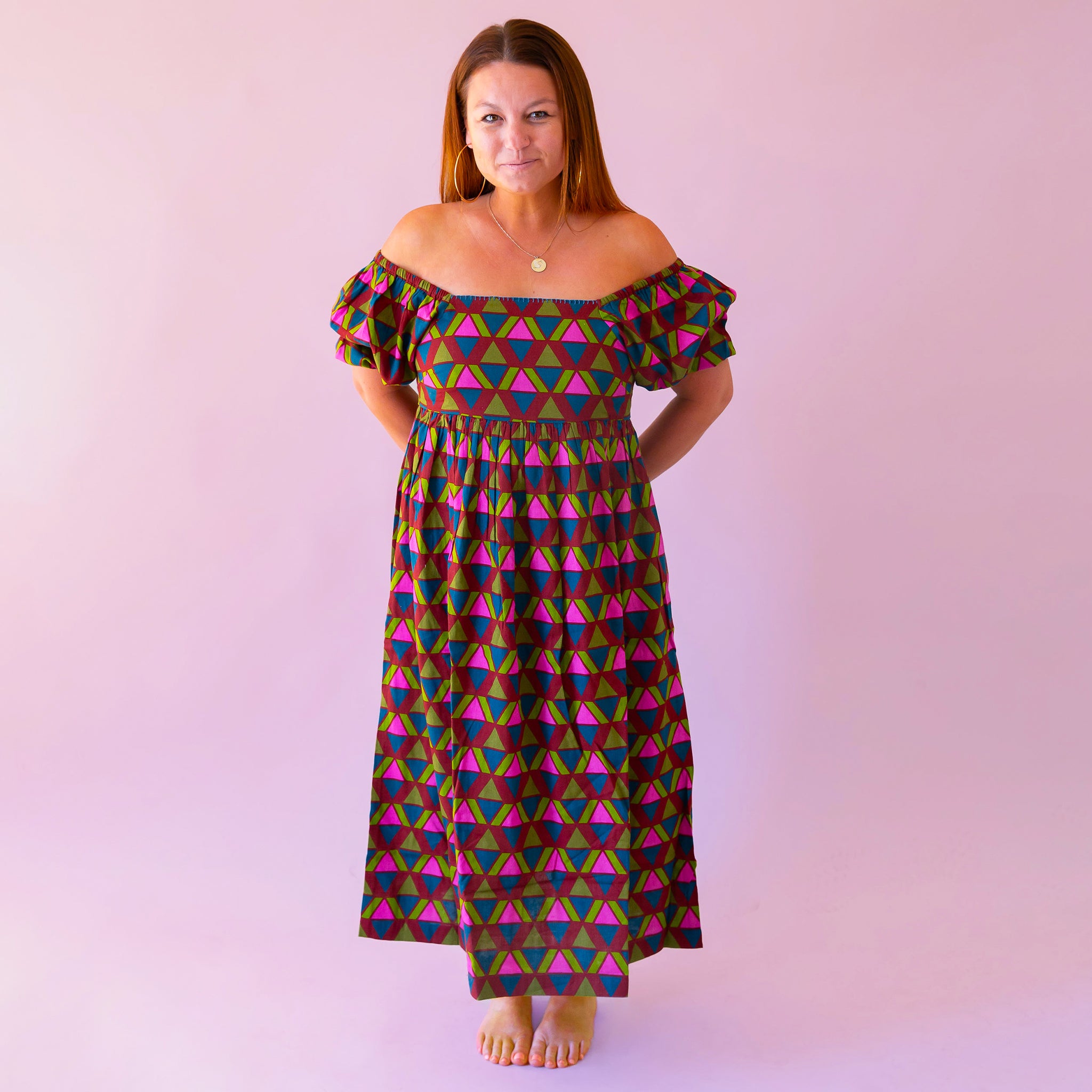 A pink, green, teal and red triangle patterned maxi dress with a square neckline, pockets and puff sleeves.