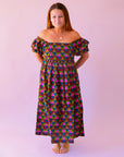 A pink, green, teal and red triangle patterned maxi dress with a square neckline, pockets and puff sleeves.