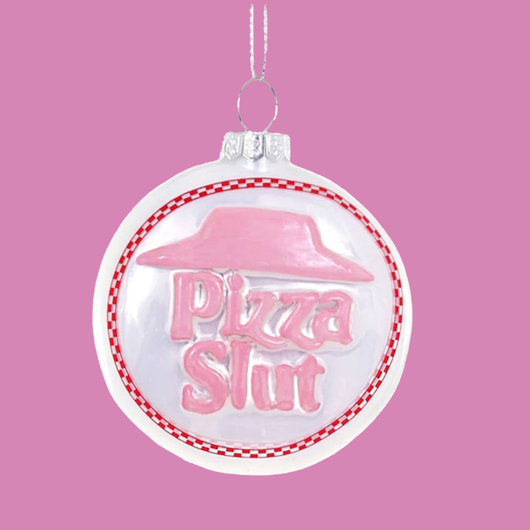 On a peach background is a white and light pink circle ornament with text in the center that reads, &quot;Pizza Slut&quot;.