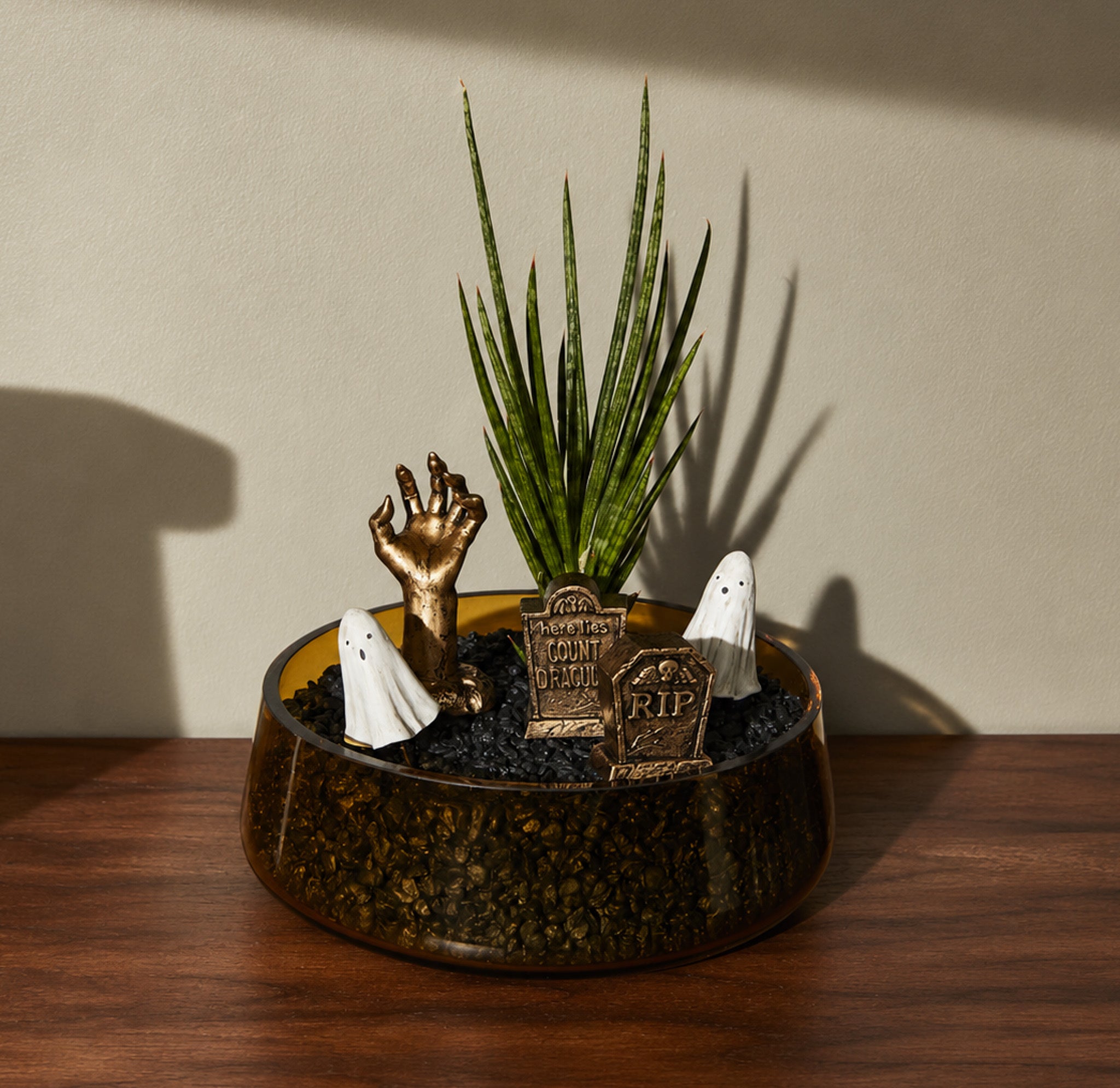Halloween themed plant stakes in a planting with black rocks on a wooden table.