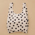 A cream and black polka dot nylon tote bag.