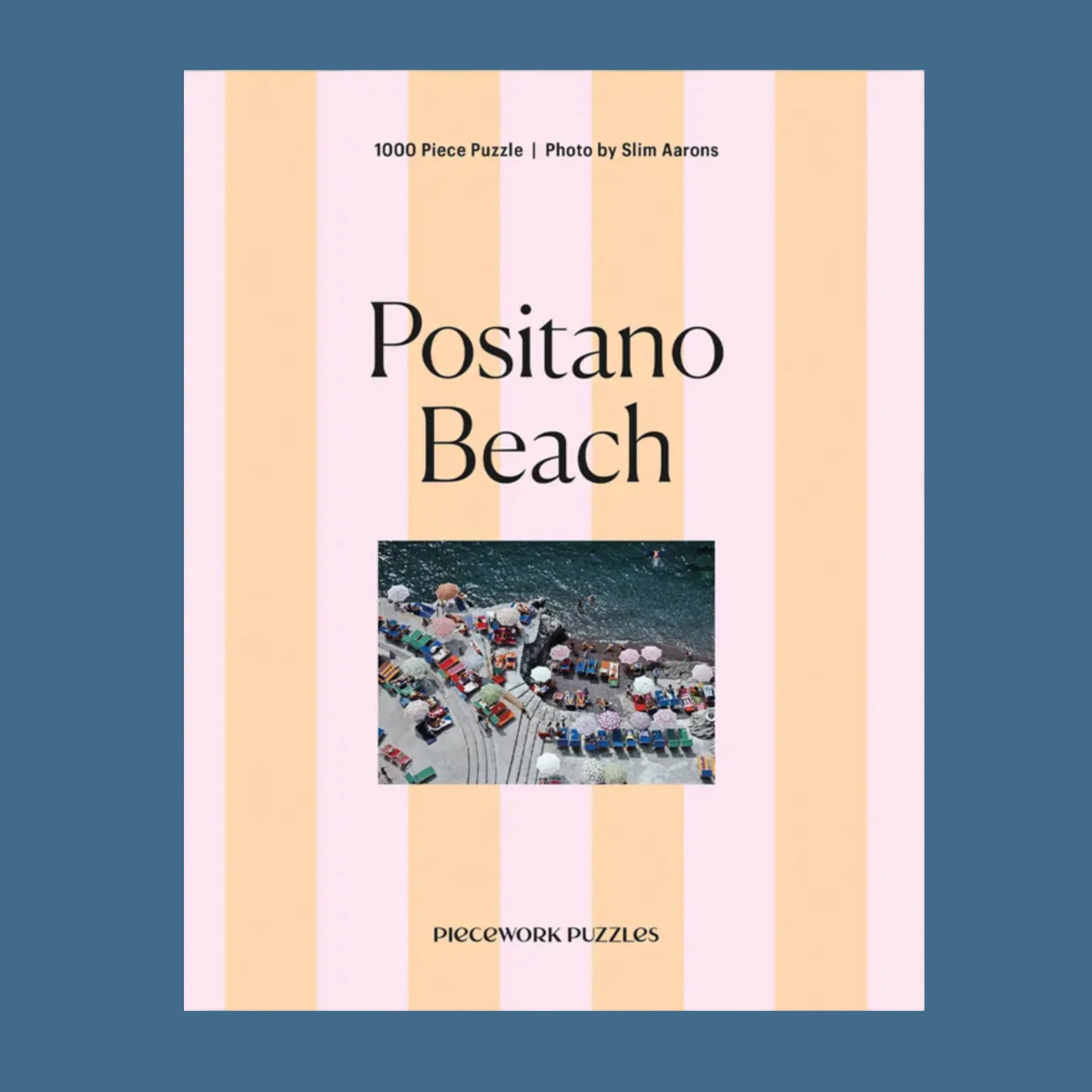 An apricot and light pink striped puzzle box with a photo of an Italian beach scene and text that reads, 'Positano Beach Piecework Puzzles'. 