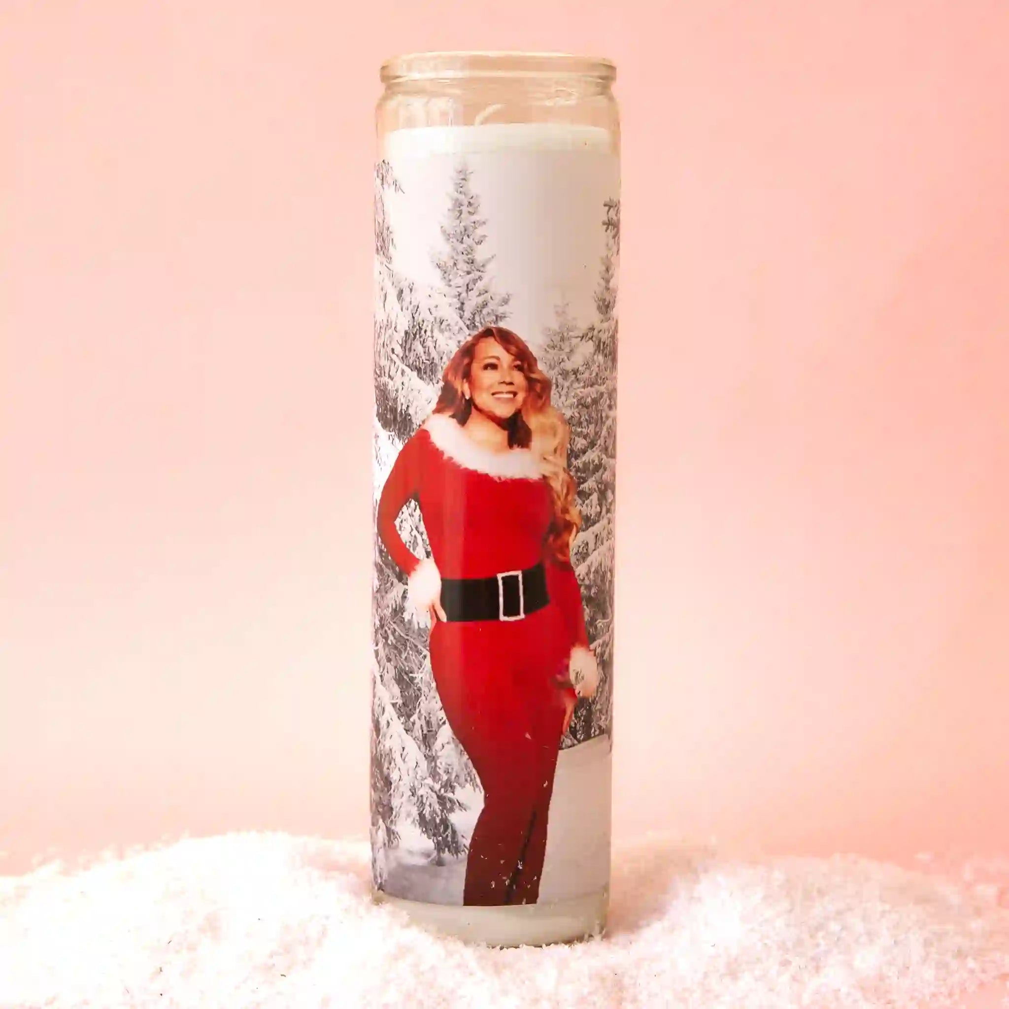 On a pink background is a thin prayer candle with a photo of Mariah Carey in a red Christmas outfit. 