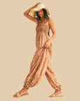 A taupe balloon leg jumpsuit with spaghetti shoulder straps and an ivory print. 