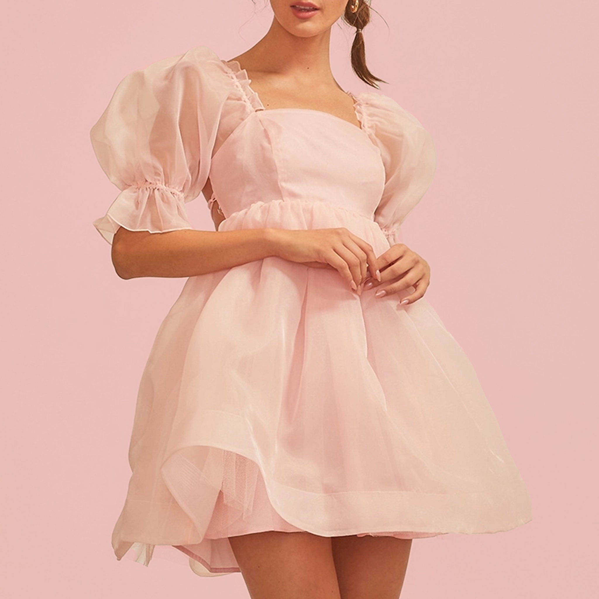 On a pink background is a model wearing a light pink puff sleeve dress. 