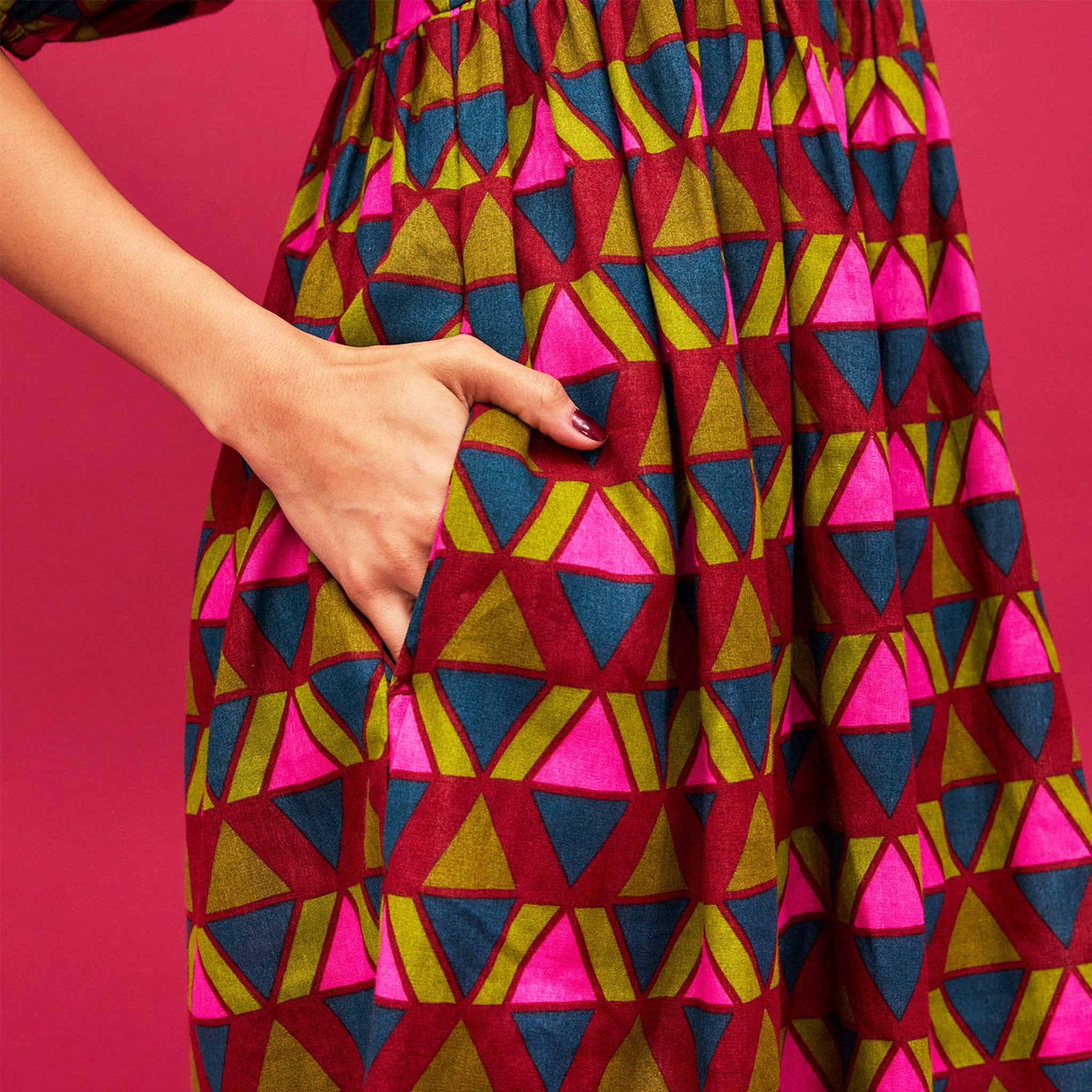A pink, green, teal and red triangle patterned maxi dress with a square neckline, pockets and puff sleeves.