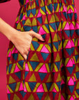A pink, green, teal and red triangle patterned maxi dress with a square neckline, pockets and puff sleeves.