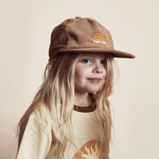 A children's model wearing a tan corduroy hat with a yellow sun logo and white text below it that reads, "rad kid".