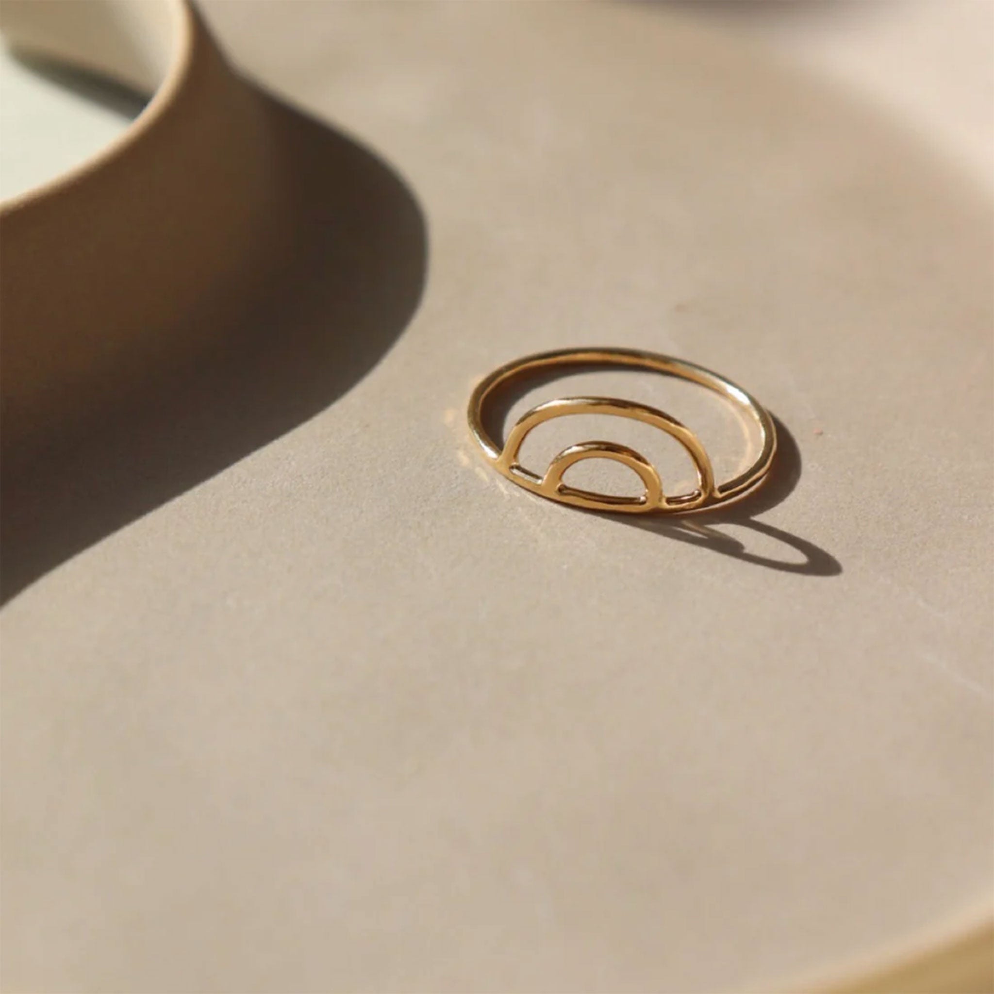 On a tan background is a dainty gold rainbow arched ring. 