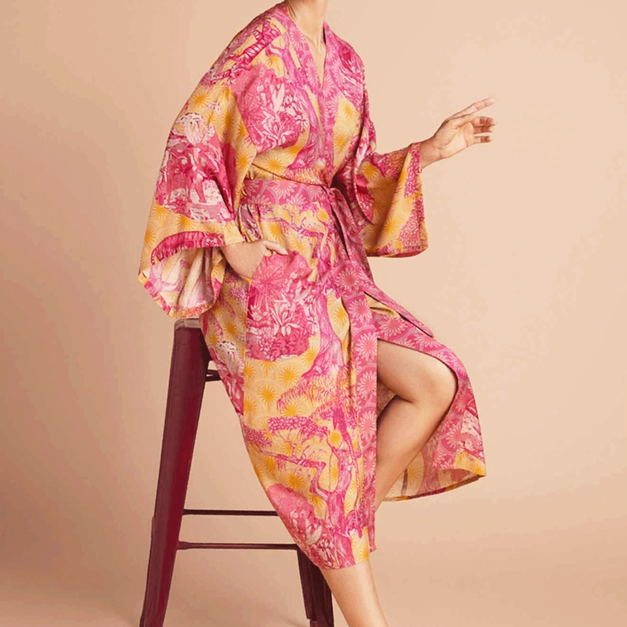 On a tan background is a model wearing a pink and yellow/orange robe with a tropical and floral print.
