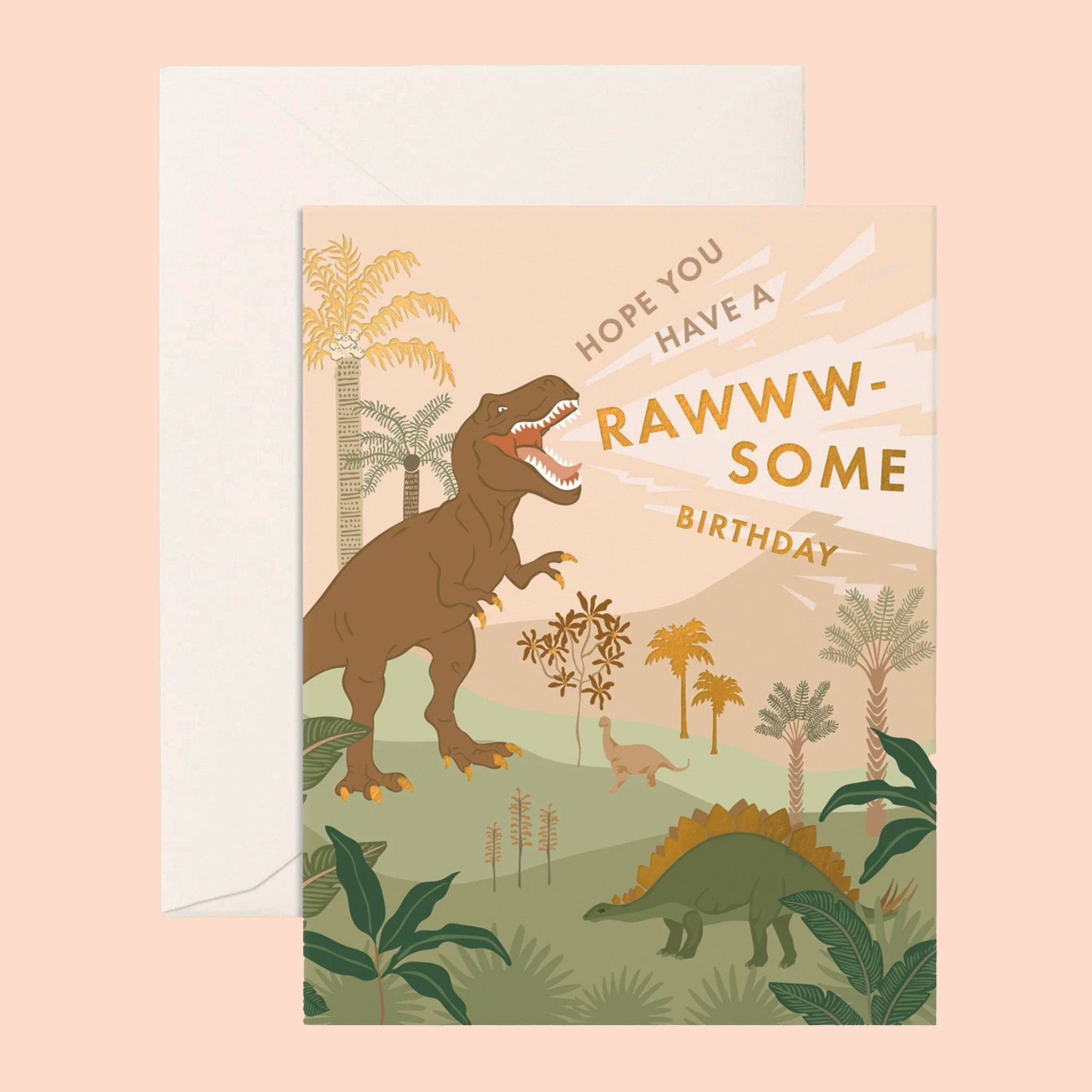 On a peachy background is a birthday card with a graphic of dinosaurs in a tropical landscape with gold foiled text that reads, "Hope You Have A Rawww-Some Birthday".