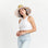 On a white background is a neutral colored straw sun hat with a neckstrap and a light pink and light orange sun design on the underside of the brim. 