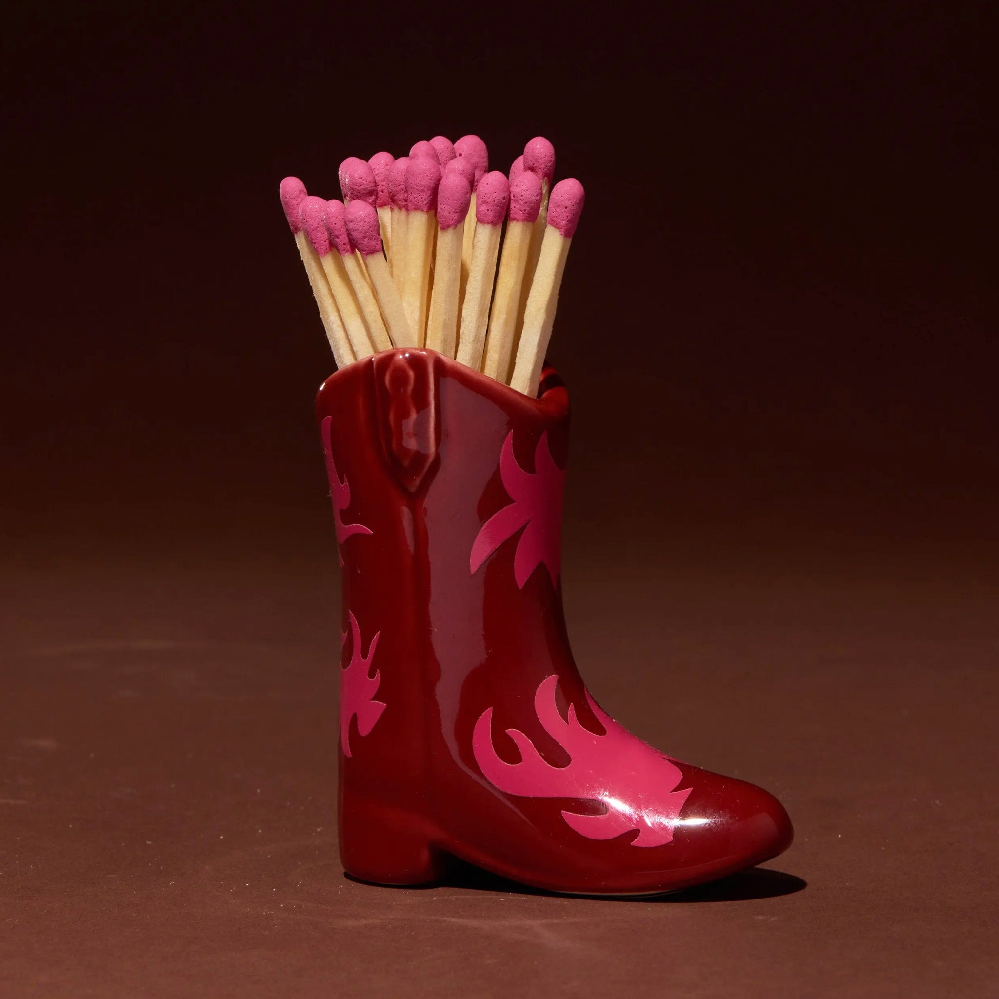 A red ceramic match holder in the shape of a cowboy boot. 