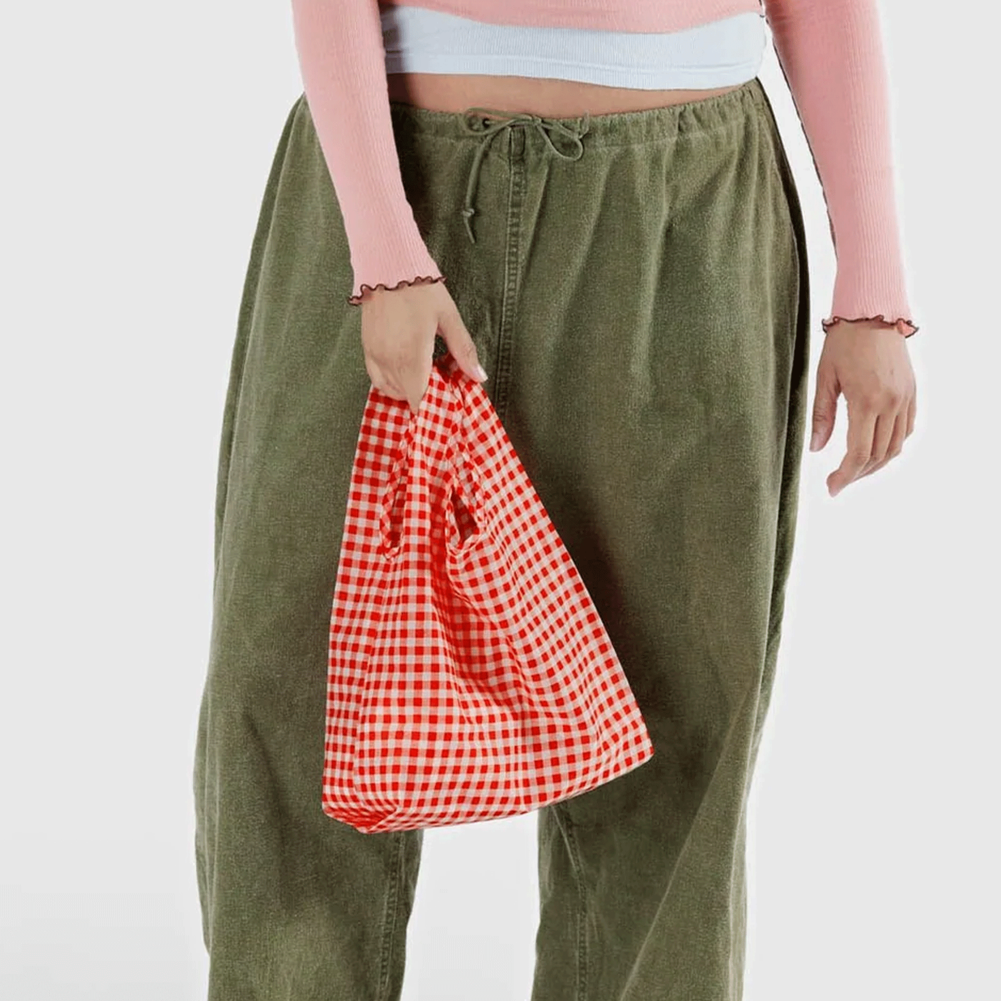 On a white background is a model holding a red gingham printed nylon tote bag. 