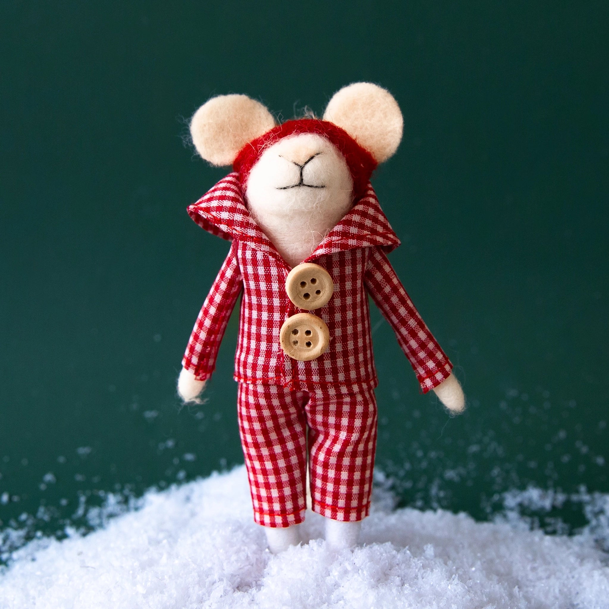On a green snowy background is a white mouse felt ornament with a red and white gingham outfit.