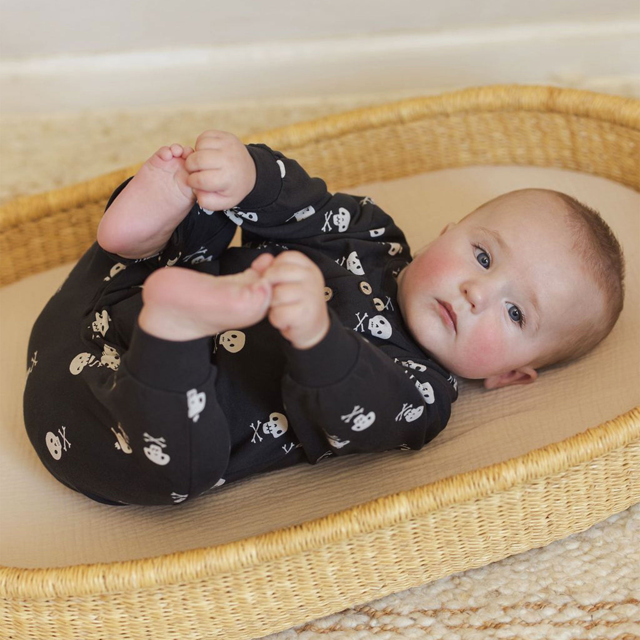 Baby wearing a black long sleeve jumpsuit with a skull and crossbones print. 
