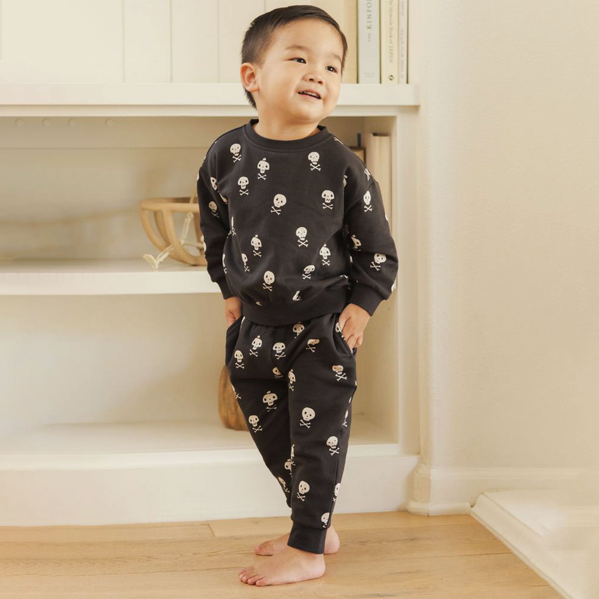 Little boy modeling a black sweatsuit with white skull and crossbones print. 