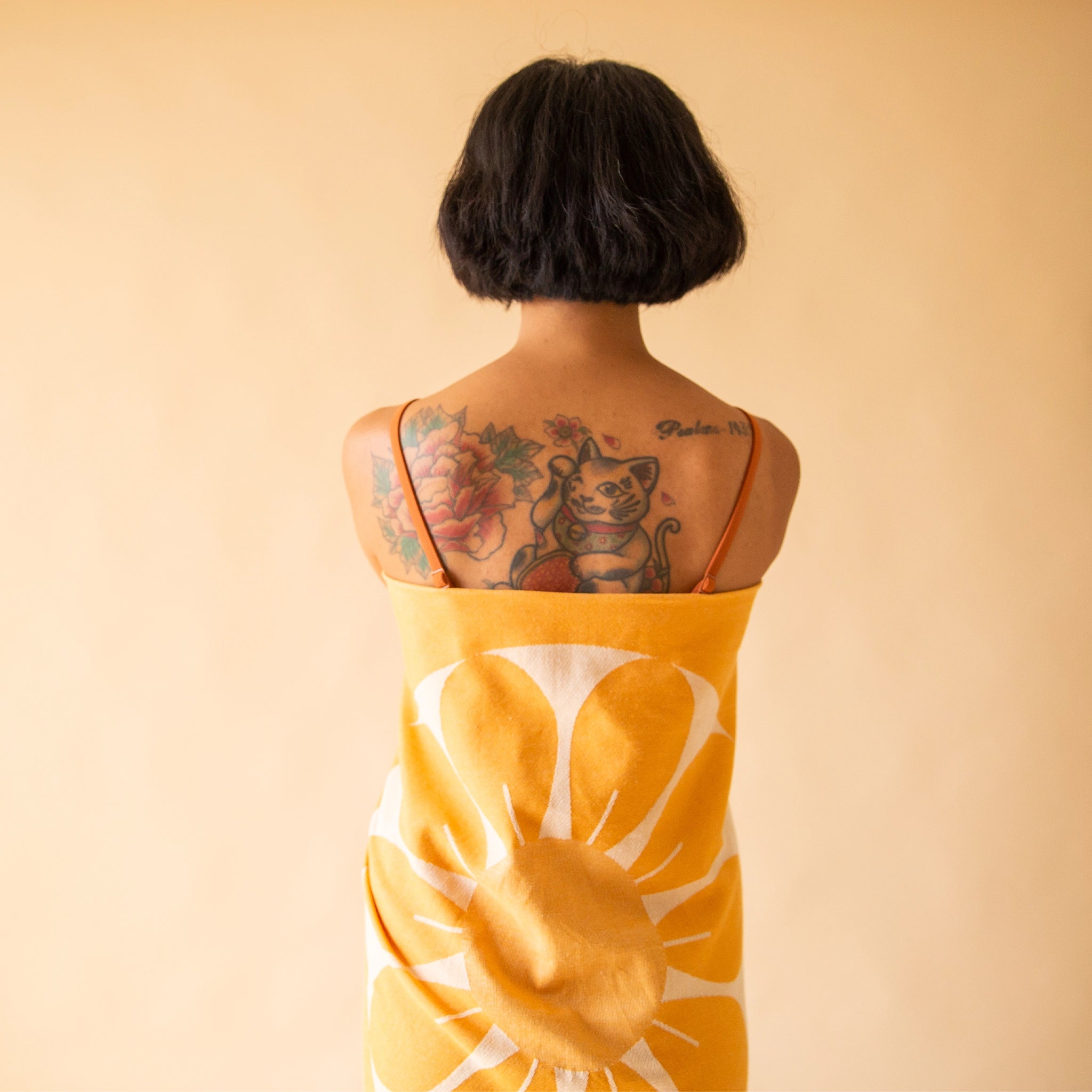 A model in front of a light orange background wearing the Retro Flower Beach Towel around their back to show the retro flower design on the towel. 