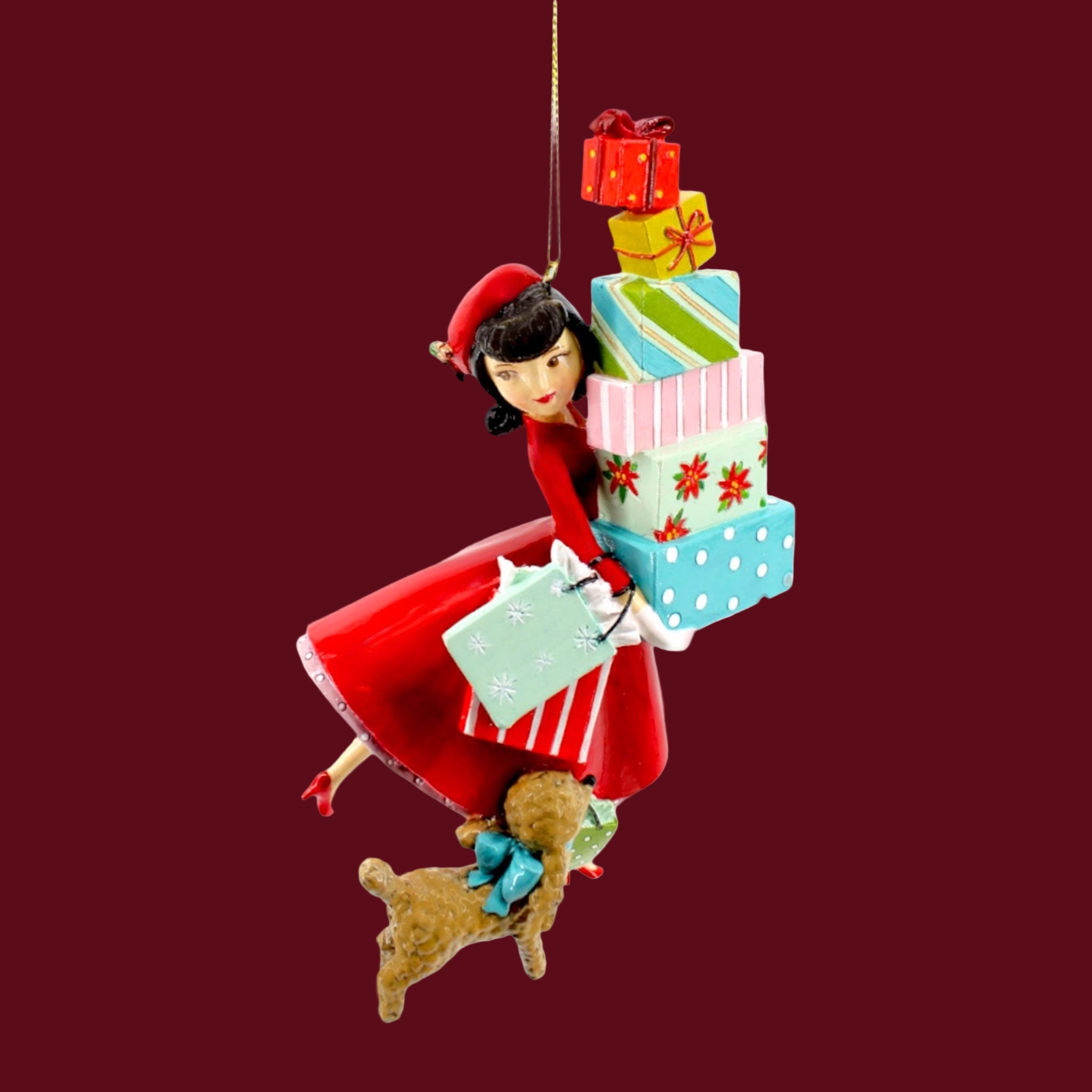 A resin ornament of a lady in a red dress with black hair holding lots of Christmas packages and a brown dog at her side.