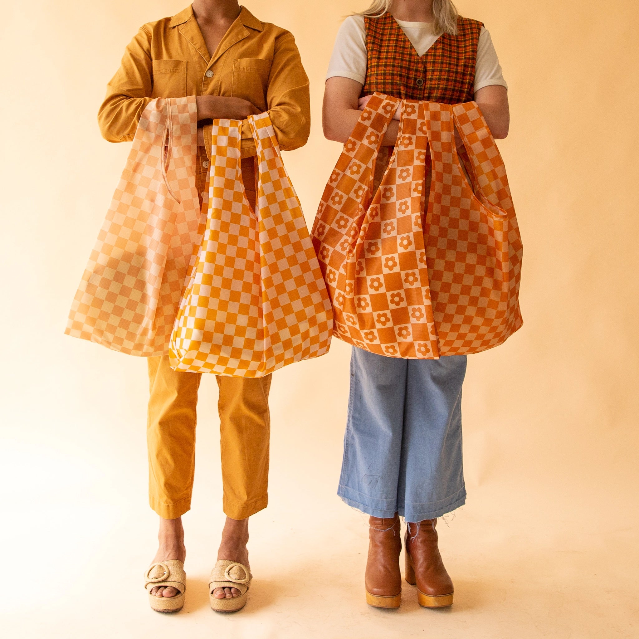 On a light orange background is a model holding the reusable bags. From left to right the models are holding, Dune Checkered, Marigold Checkered, Flower Checkered, and Playa Checkered.