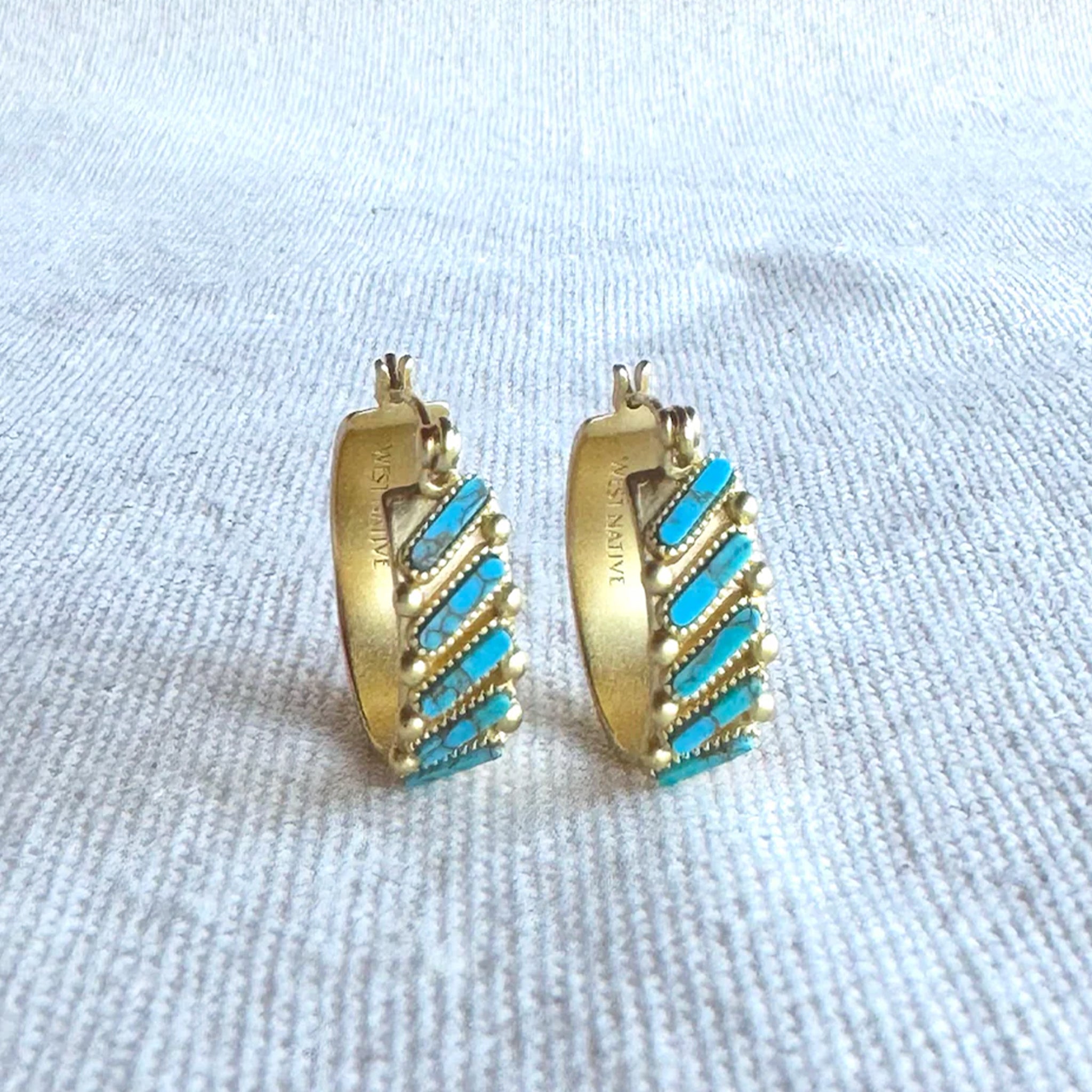 A gold pair of hoop earrings with turquoise stones. 