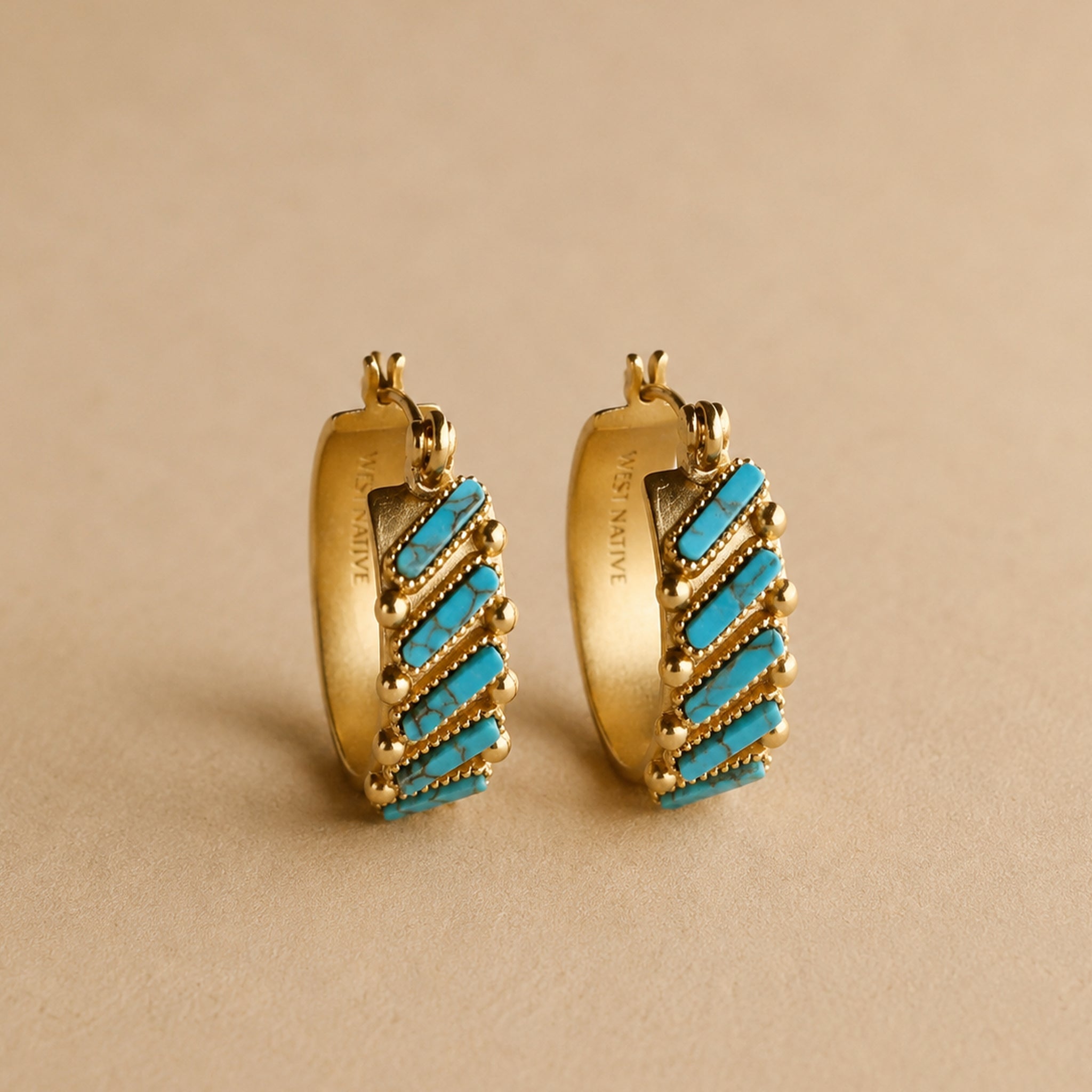 A gold pair of hoop earrings with turquoise stones. 
