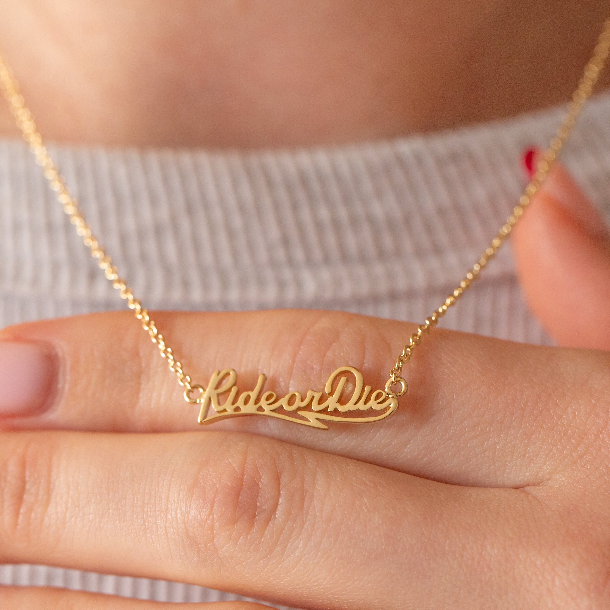 A gold nameplate style necklace with text that reads, "RideorDie". 