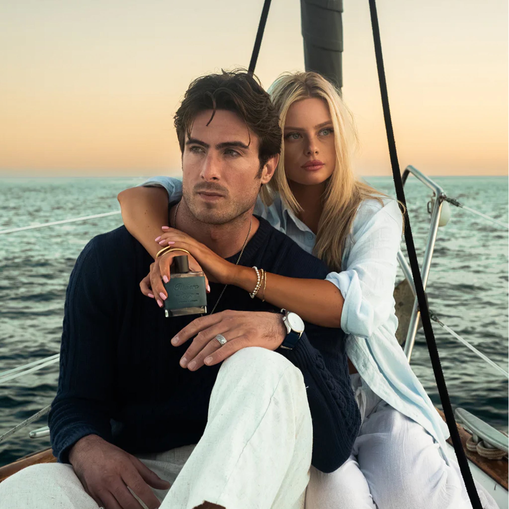 Man and woman sitting on a boat with a scenic ocean view holding the cologne bottle