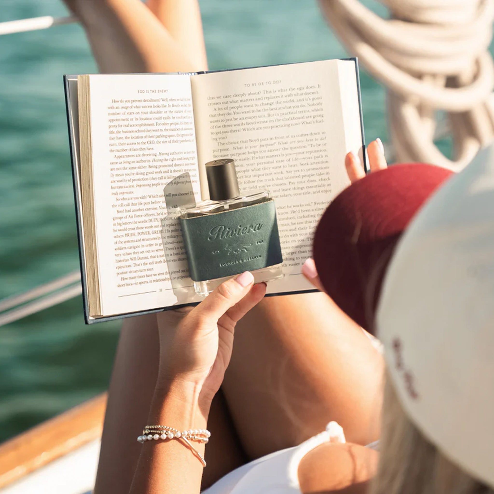 Person reading a book with a bottle of Nuxe perfume on a boat
