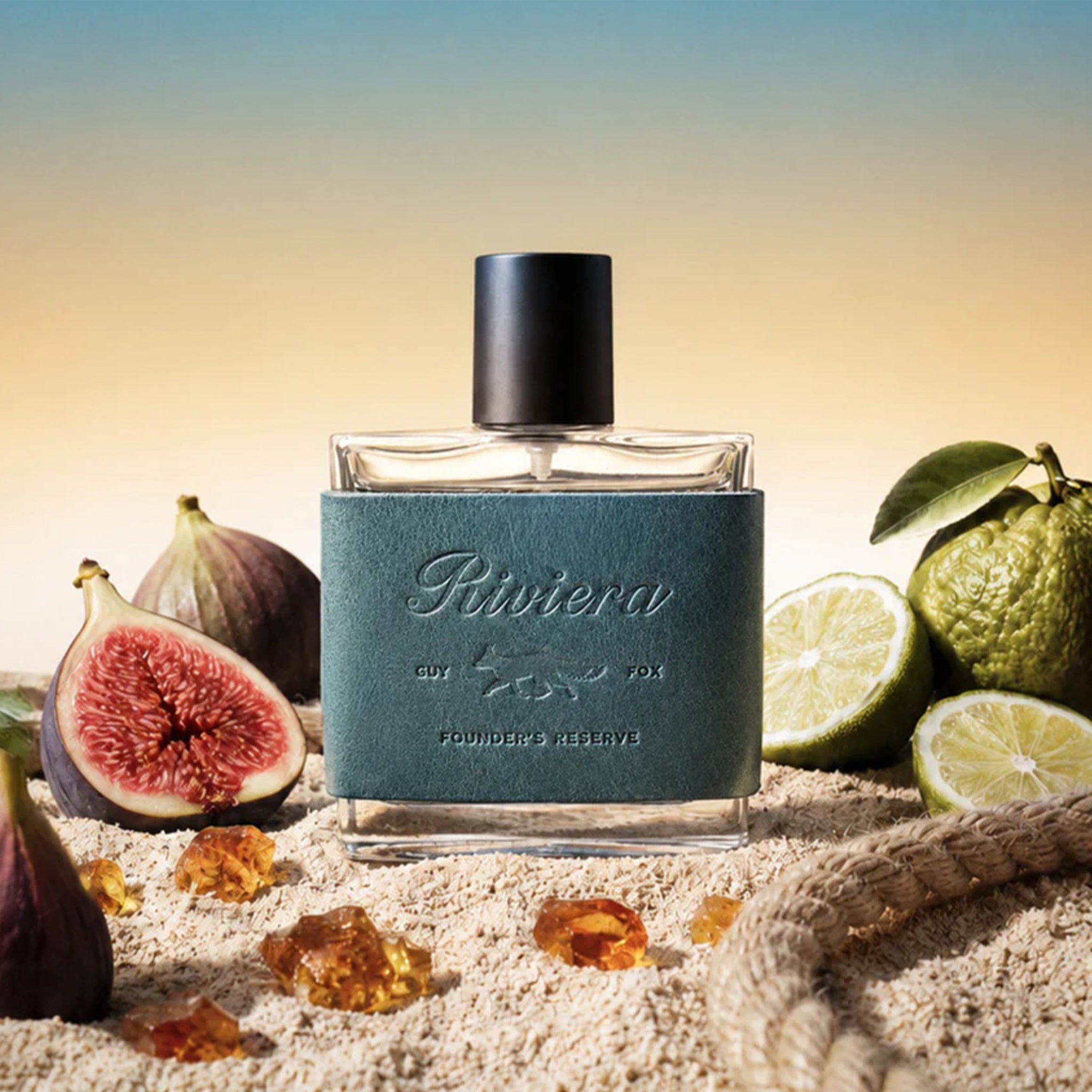 Perfume bottle labeled 'Riviera' with figs, limes, and amber on a sandy background