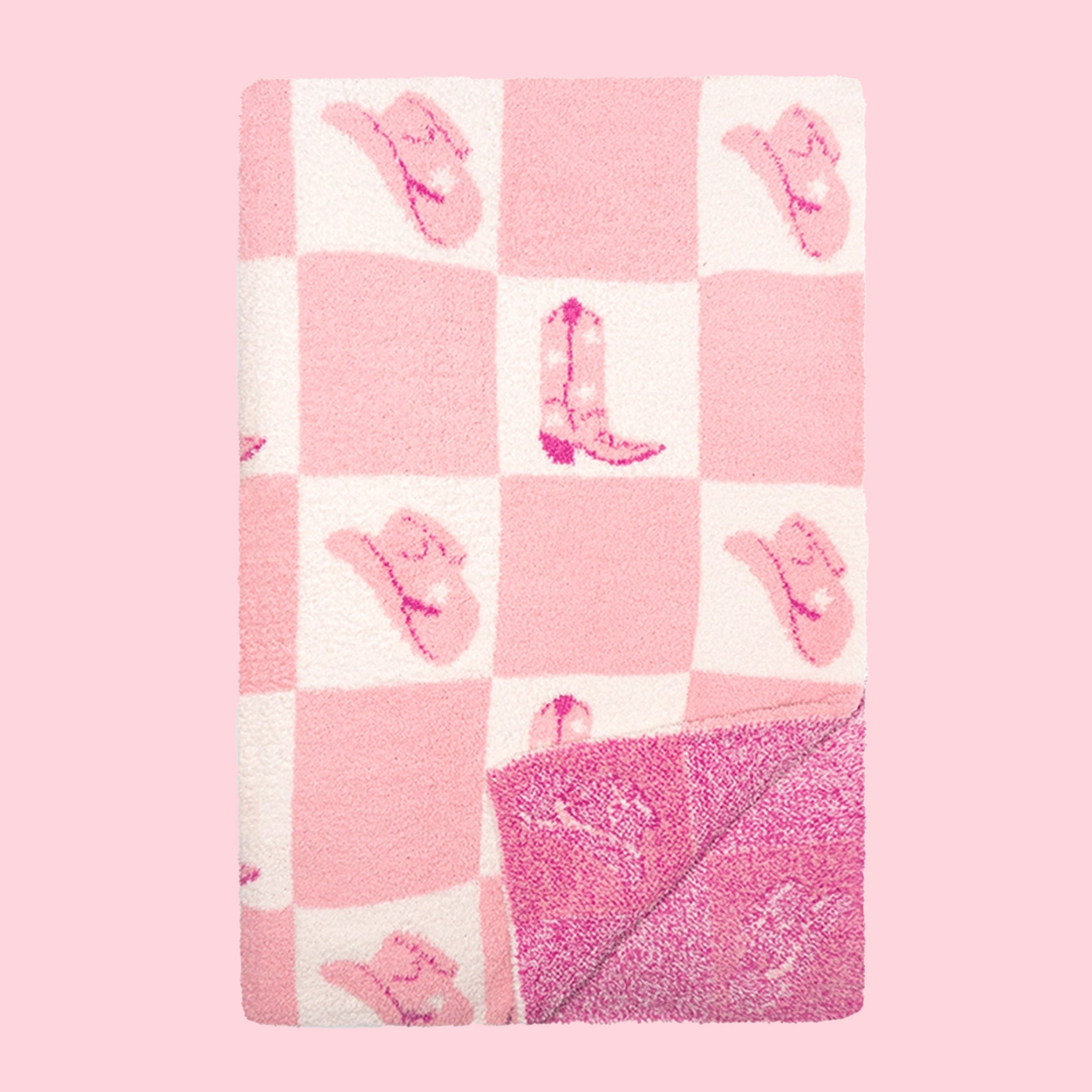 On a pink background is a folded pink and white checkered blanket with alternating pink cowgirl hats and cowgirl boots in each white square.