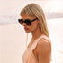 A black oversized round pair of sunglasses with a reddish brown lens. 