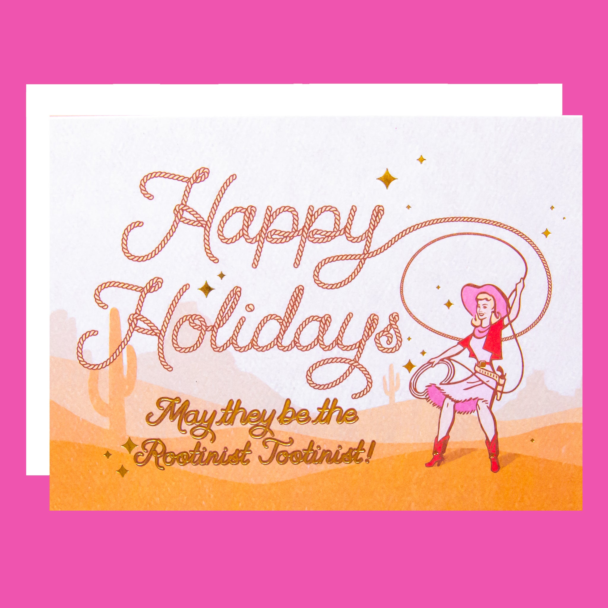 Cowgirl swinging a lasso with rope style font that reads "Happy Holidays May they be the rootinist tootinist!" There is a cactus and mountain range background behind her.  Card is laying on a pink background paper.