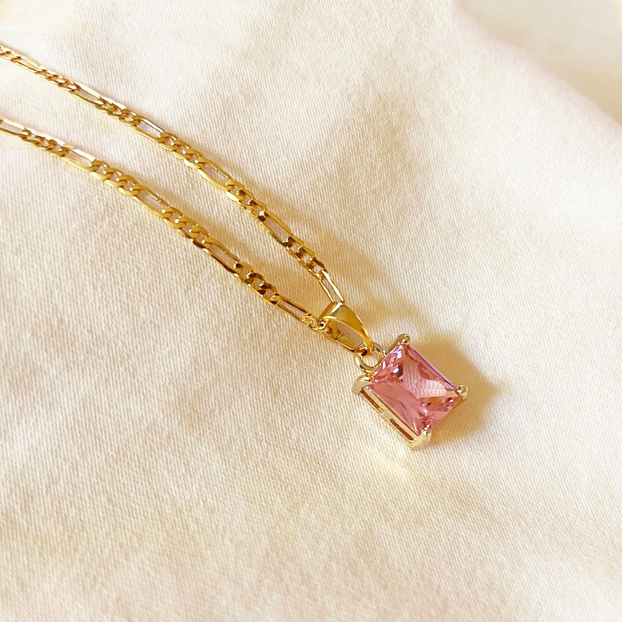 Gold necklace with a pink gemstone pendant on a beige fabric background