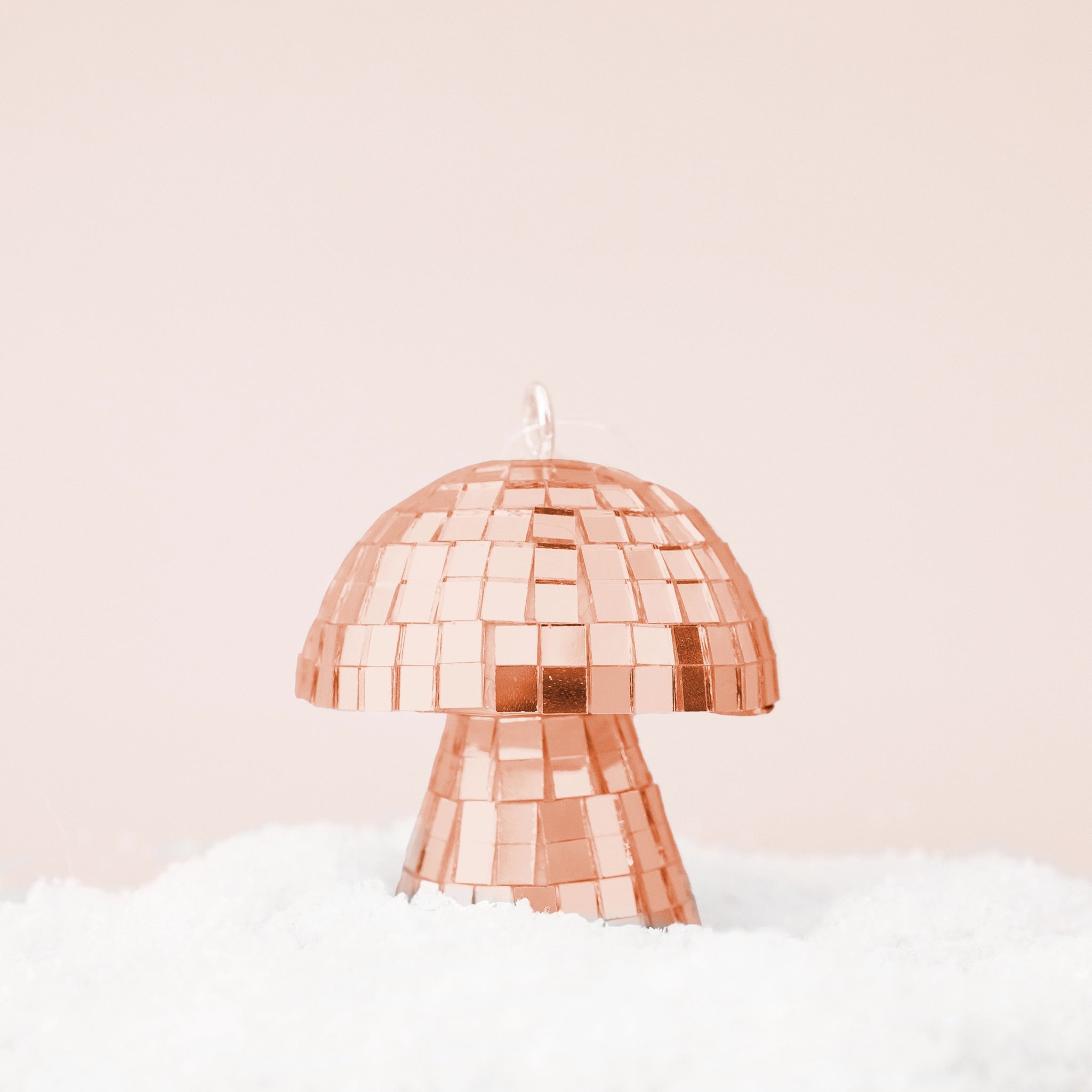 On a neutral snowy background is a rose gold disco mushroom shaped ornament.