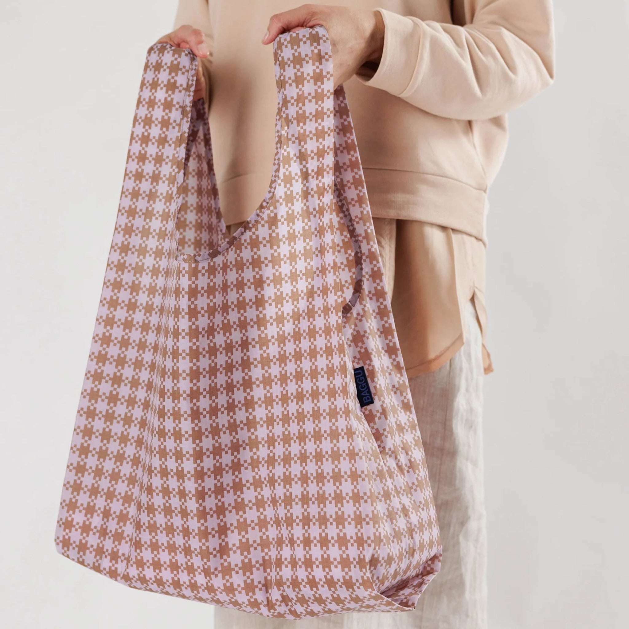 On a white background is a rose colored reusable tote with a gingham print all over.