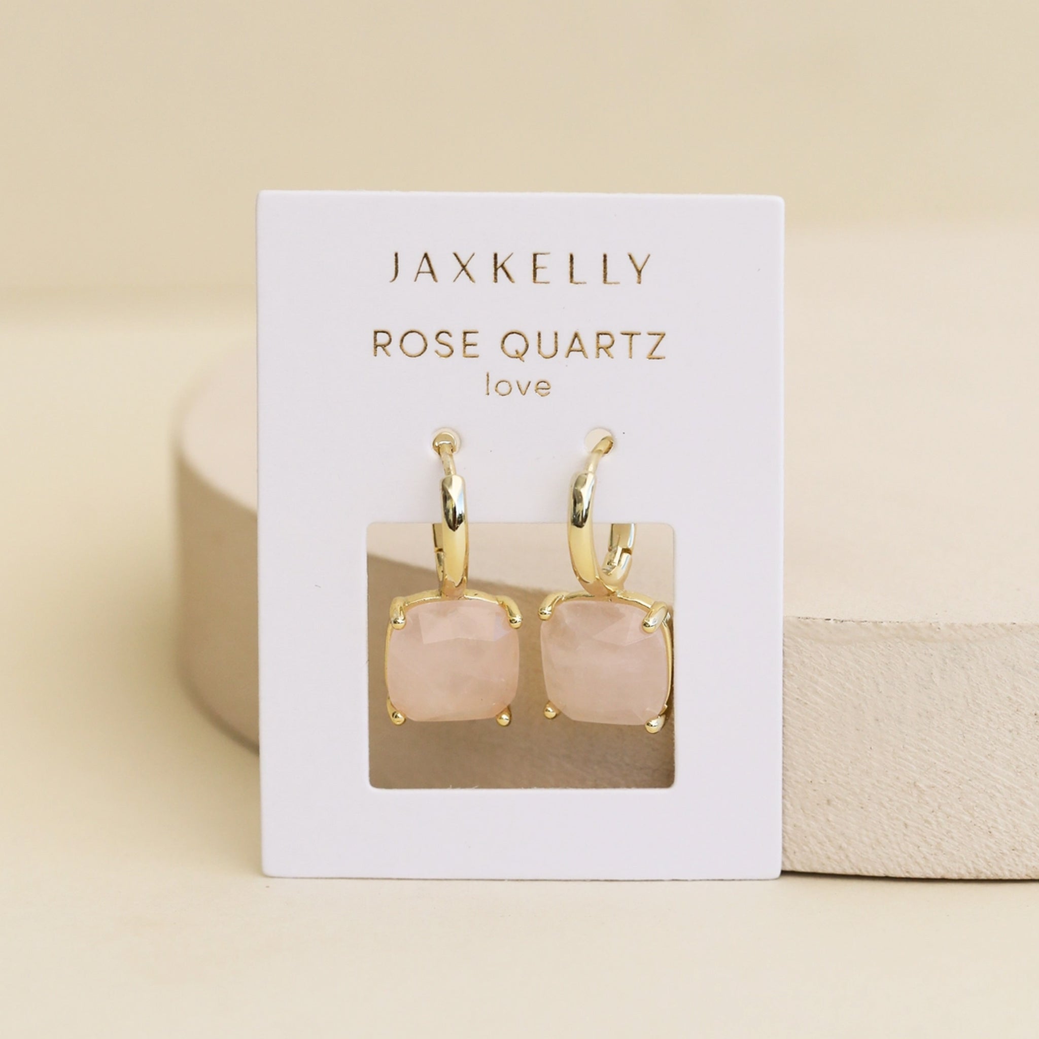 A gold pair of hoop earrings with light pink rose quartz stones. underneath. 