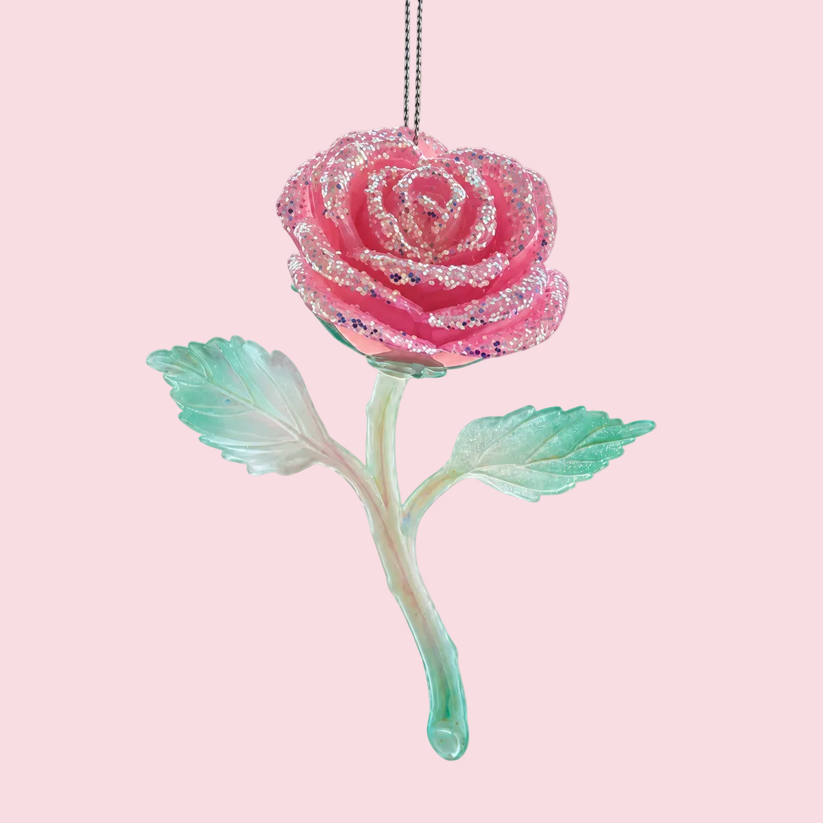 A hanging ornament shaped like a rose, with a glittery pink flower head, pale mint green stem, and two mint green leaves against a solid pink background.