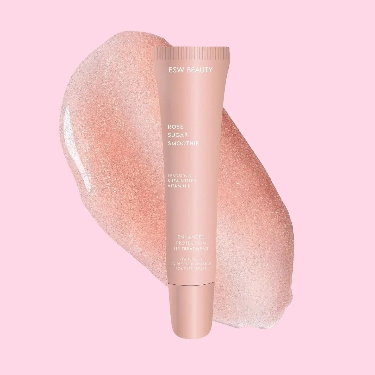 Pale pink ESW Beauty ‘Rose Sugar Smoothie’ lip treatment tube centered over a shimmering rose-gold swatch on a pastel pink background.