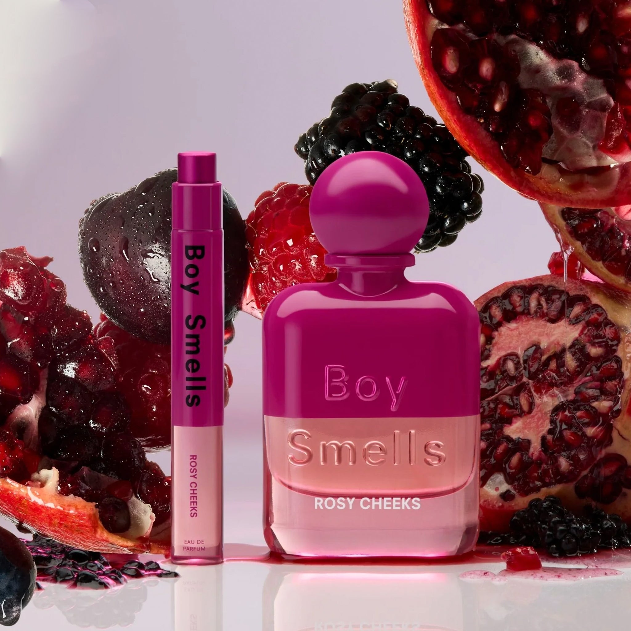 A hot pink and clear bottle of perfume with a round cap and text that reads, 'Boy Smells Rosy Cheeks'. 
