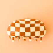 On a peach background is a brown and ivory checkered claw clip with a rounded edge.
