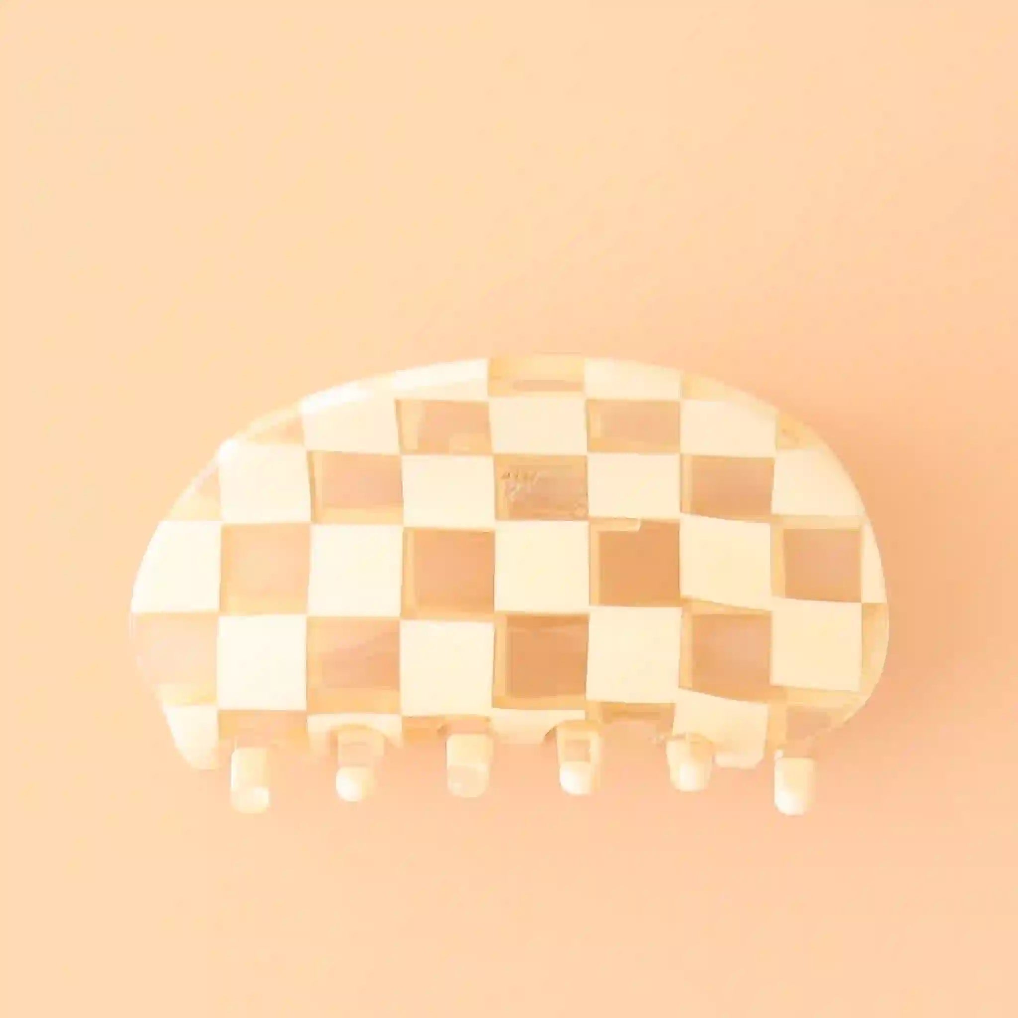 On a peachy background is an ivory and clear checker printed claw clip with a rounded edge.