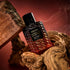A reddish/black ombre bottle of perfume with black details and a black label that reads, 'Voluspa Saddle Up Santal'.
