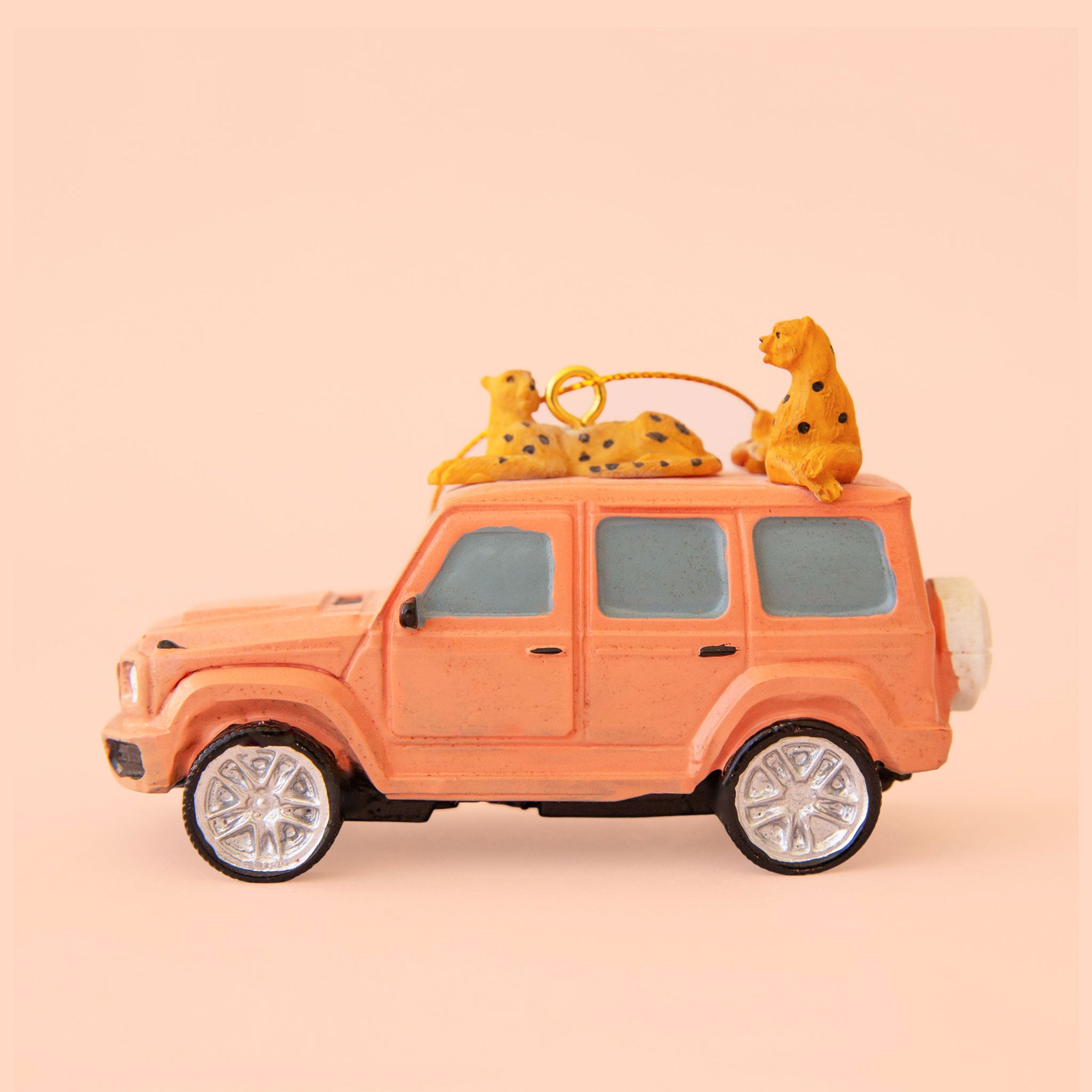 Peach safari car ornament with two cheetahs perched on the roof of the car. 